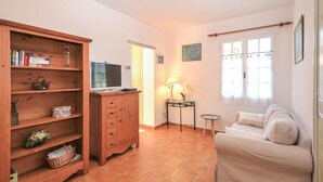 Una sala de estar acogedora con una estantería de madera, un televisor, una mesita con una lámpara y un sofá.
