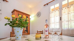 Un comedor con una mesa lista para dos personas, un jarrón de rosas amarillas, una botella de vino y un armario de madera al fondo.