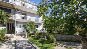 Un edifici residencial de diversos pisos amb balcons, una zona de jardí amb diverses plantes i un camí pavimentat que condueix a l'entrada.