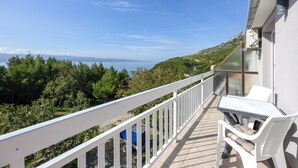 Un balcó amb barana blanca que ofereix vistes a un paisatge costaner amb arbres i el mar.