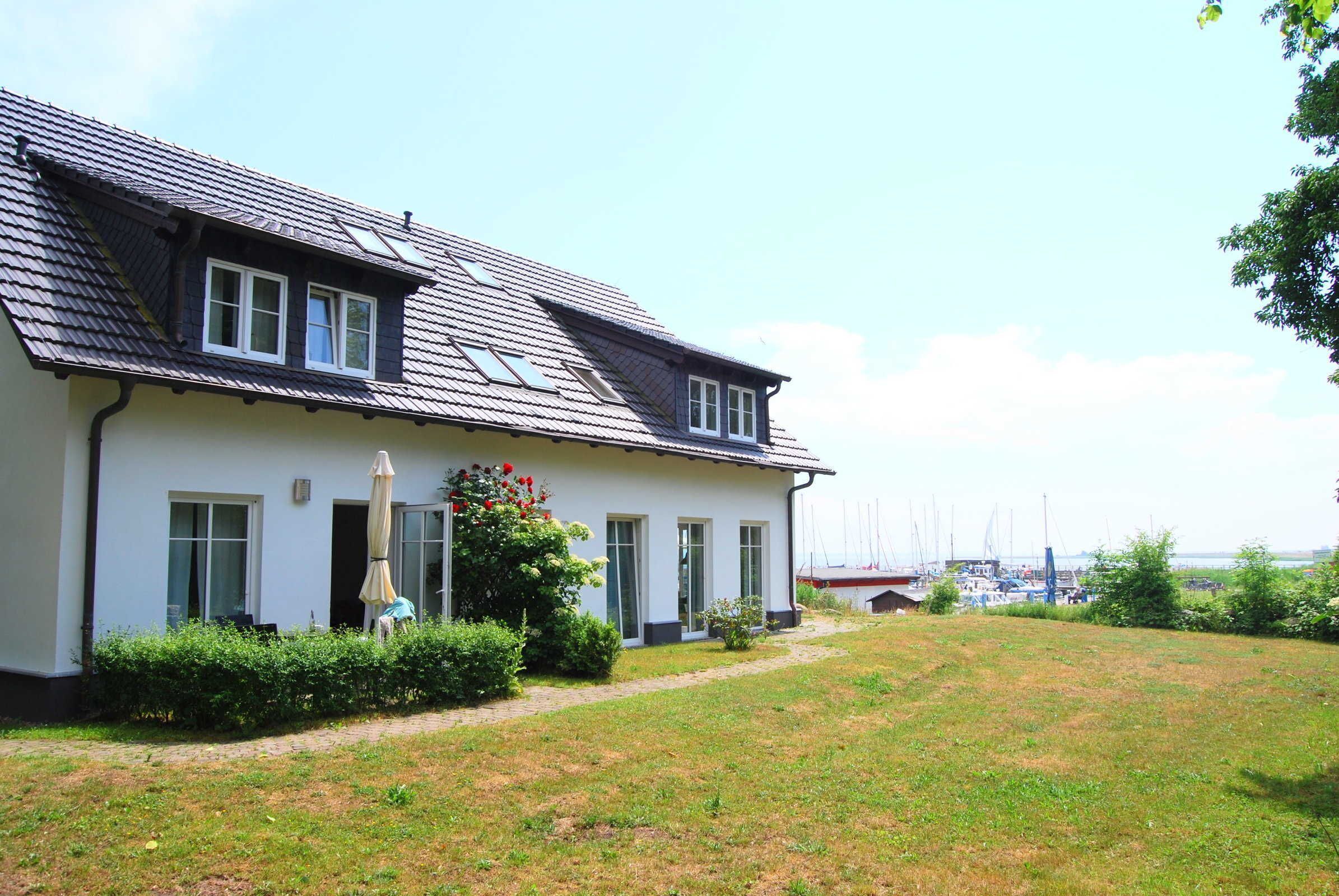 A two-story house with a sloped roof, a covered patio, and a view of a marina with boats.