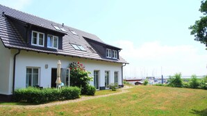 A two-story house with a sloped roof, a covered patio, and a view of a marina with boats. - Hitthim apartment rental - Apartment harbor view (Insel Hiddensee)