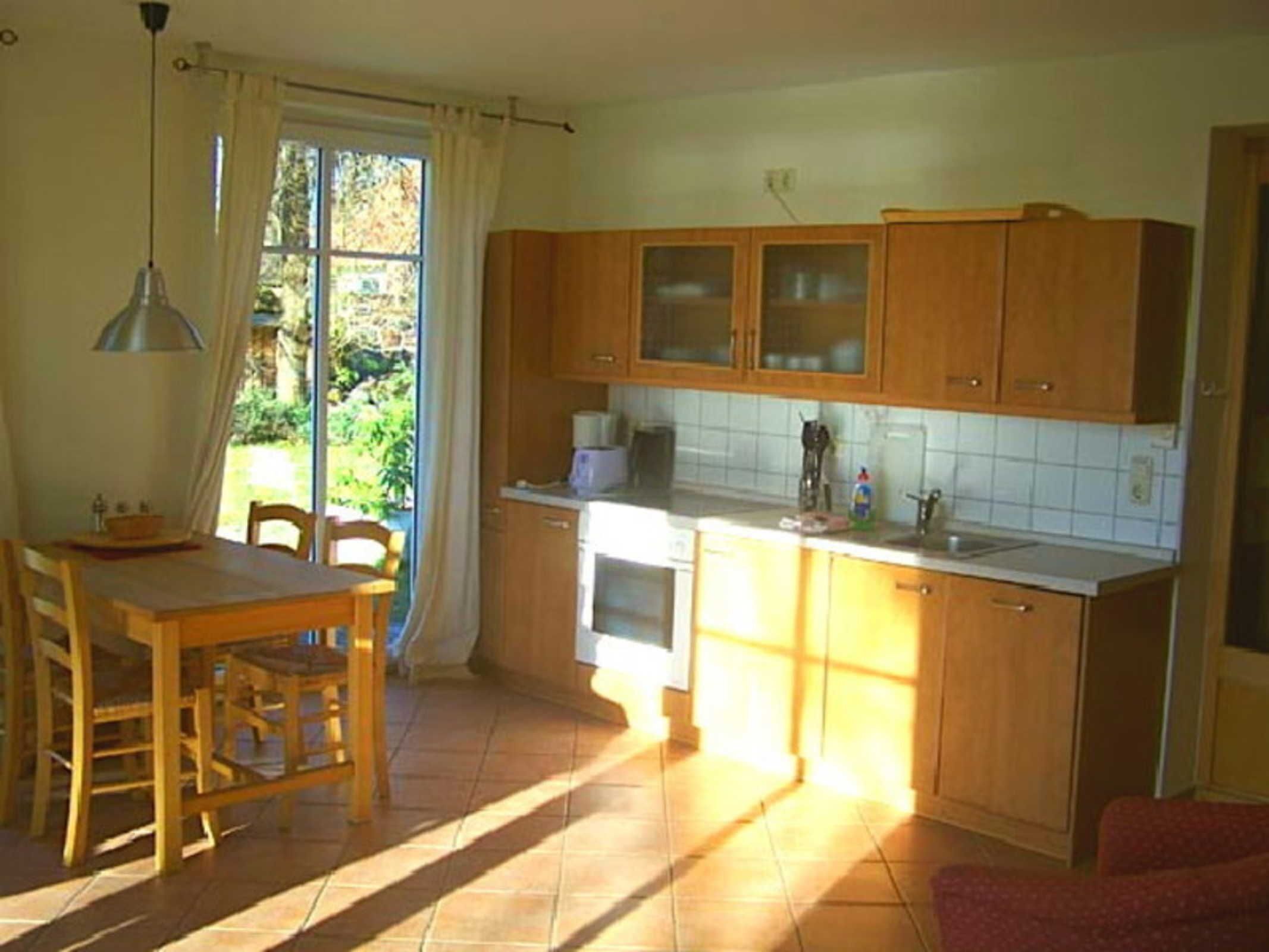 A kitchen with wooden cabinets, a dining table, chairs, and a window with curtains.