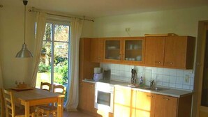 A kitchen with wooden cabinets, a dining table, chairs, and a window with curtains. - Hitthim apartment rental - Apartment harbor view (Insel Hiddensee)