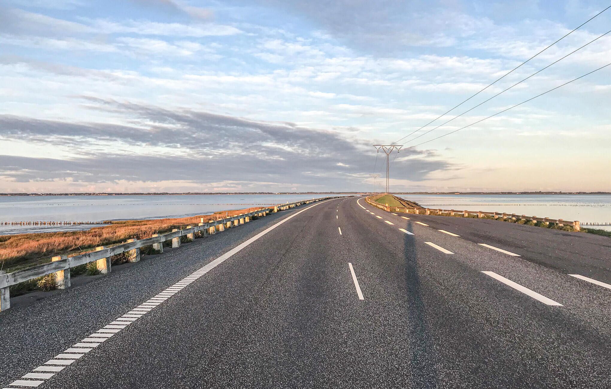 A coastal road with a guardrail, clear skies, and a view of the sea.