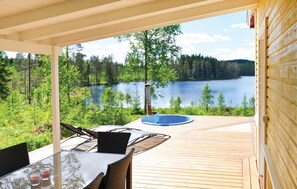 Una terrazza coperta all'aperto con un tavolo e sedie in vetro, con vista su un lago e una foresta.