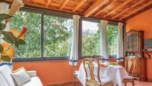 A dining area with a wooden table and chairs, a white sofa, and a view of trees through large windows. - Lovely home in Colle di Compito LU (Colle di Compito LU)