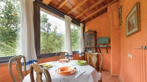A dining area with a table set for two, a wooden cabinet, a television, and a window with curtains. - Lovely home in Colle di Compito LU (Colle di Compito LU)