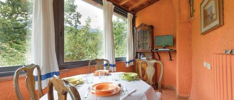 A dining area with a table set for two, a wooden cabinet, a television, and a window with curtains.