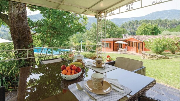 An outdoor dining area with a table set for two, a bowl of fruit, and a view of a mountain landscape. - Lovely home in Colle di Compito LU (Colle di Compito LU)