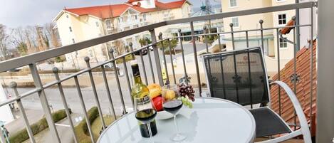 A balcony with a table set for two, a bottle of wine, and a bowl of fruit.