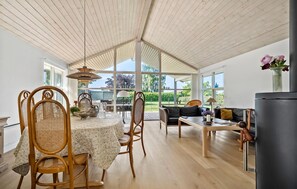 Une pièce spacieuse avec un plafond en bois, un coin repas comprenant une table et des chaises, un canapé et une vue sur la verdure à l’extérieur.