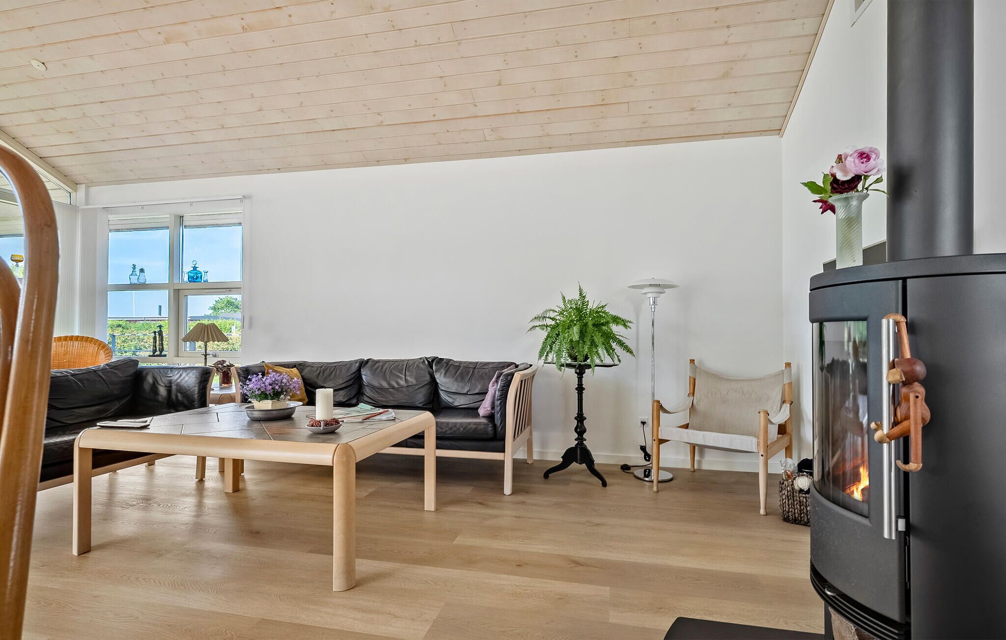 Een ruime woonkamer met houten vloer, een zwarte leren bank, een houten salontafel en een zwarte schoorsteen.