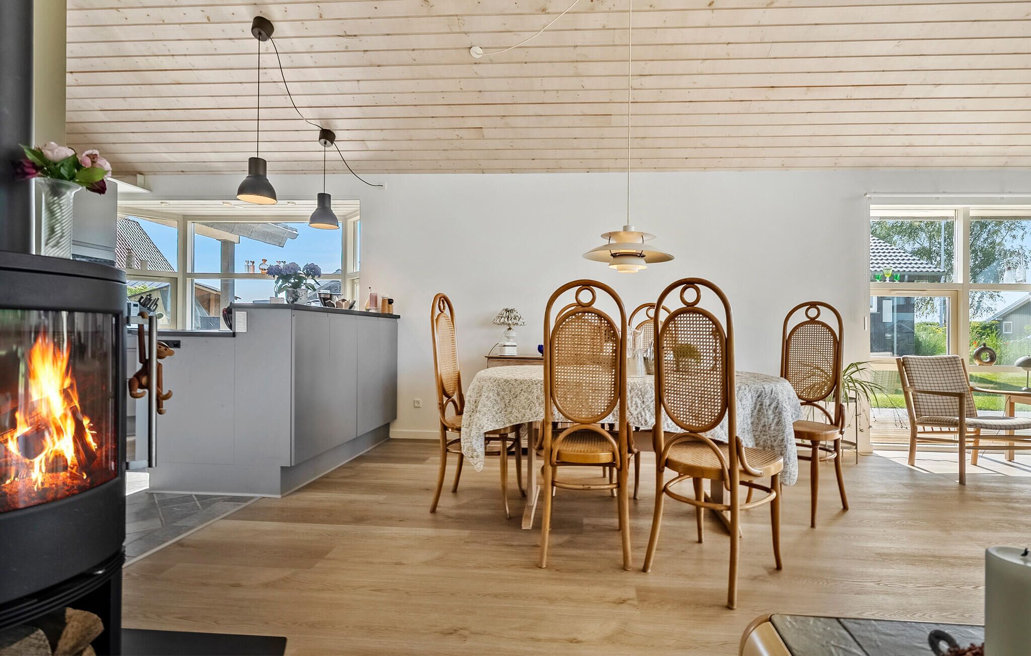 Una cocina moderna con estufa de leña, un comedor con sillas de mimbre y un amplio ventanal con vistas al exterior.