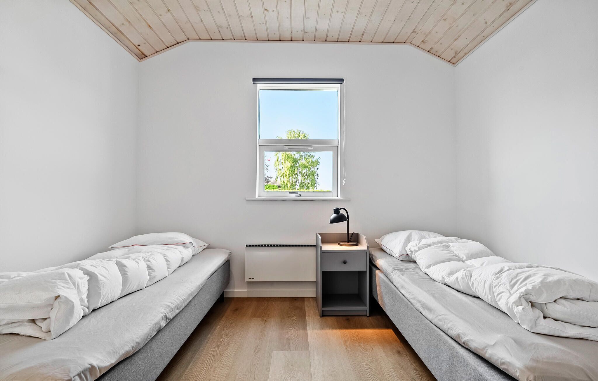 Ein kleiner, gut beleuchteter Raum mit zwei Einzelbetten, einem Schreibtisch mit Lampe und einem Fenster mit Blick auf Grün.