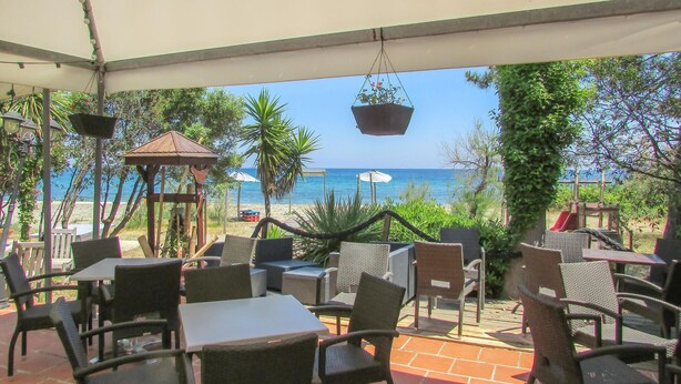 An outdoor seating area with tables and chairs, overlooking a beach and the sea. - Gorgeous apartment in Moriani Plage (Moriani Plage)