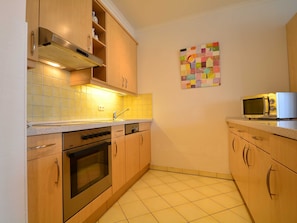 Cozinha compacta com armários de madeira, forno de aço inoxidável, micro-ondas e painel de azulejos.