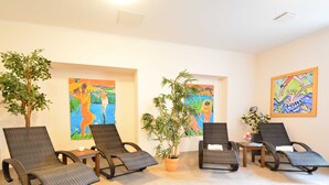 Una habitación con cuatro sillones de mimbre, dos plantas en macetas y coloridas pinturas abstractas en las paredes.