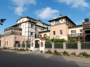 Un edificio residencial de varios pisos con un balcón, una estructura en forma de torre en el techo y una entrada con portones.