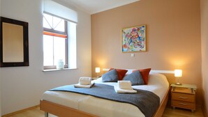 Un dormitorio moderno con una cama grande, dos mesitas de noche, una ventana con persianas y un cuadro abstracto colorido en la pared.
