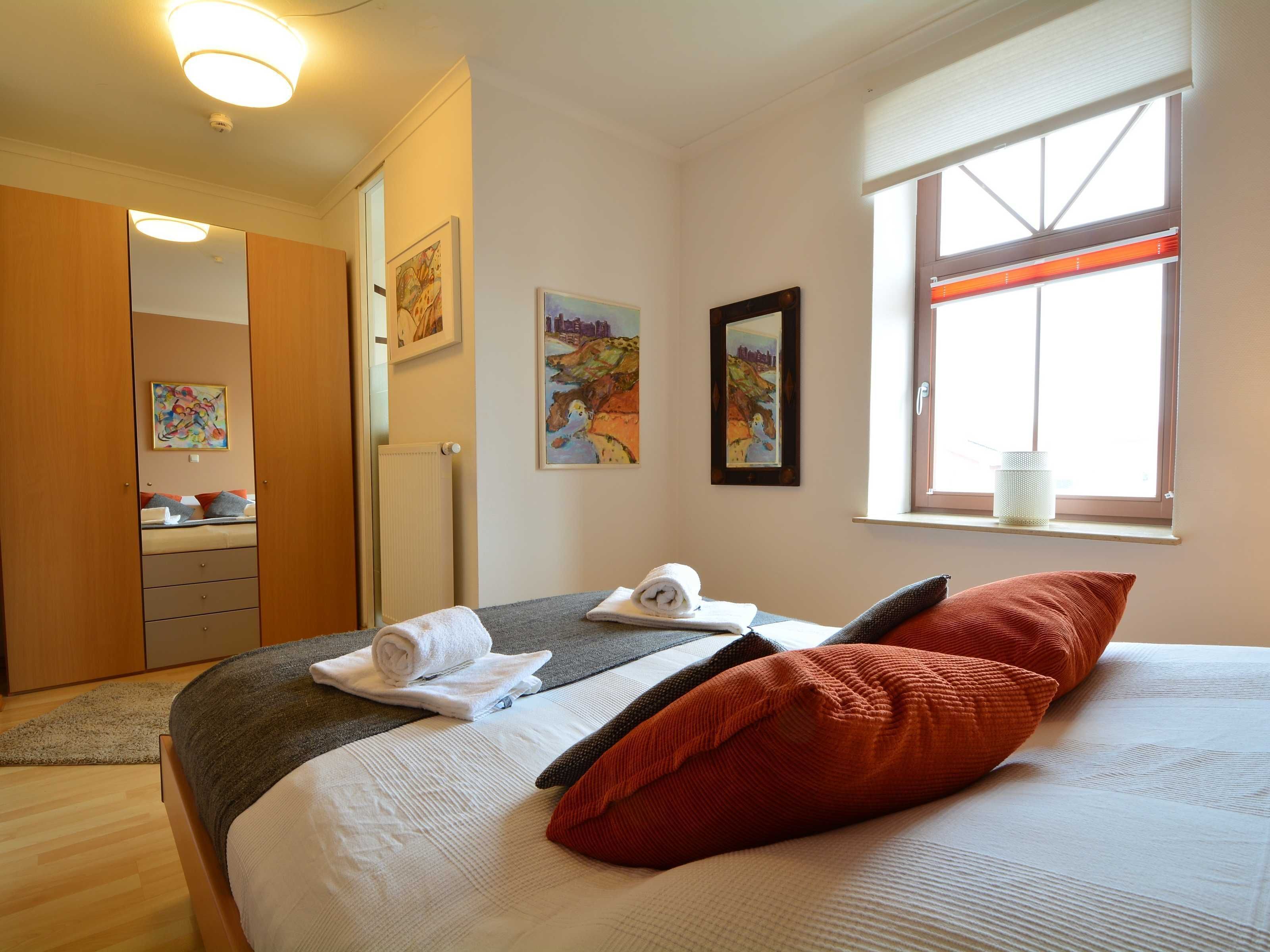 Un dormitorio con cama, ventana, radiador y cuadros en la pared.