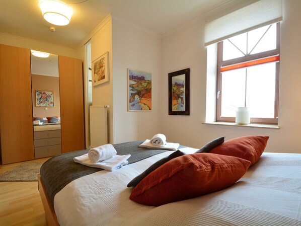 A bedroom with a bed, a window, a radiator, and artwork on the wall.