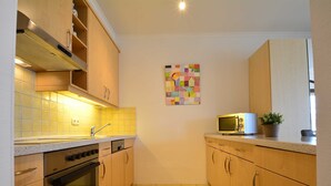 Cocina compacta con armarios de madera, horno de acero inoxidable, microondas y salpicadero de azulejos.