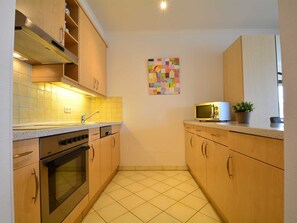A compact kitchen with wooden cabinets, a stainless steel oven, a microwave, and a tiled backsplash.