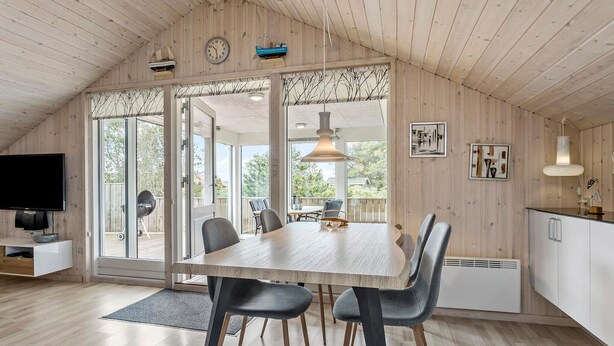 Een ruime eethoek met een grote tafel en stoelen, een televisie, en uitzicht op de omgeving.