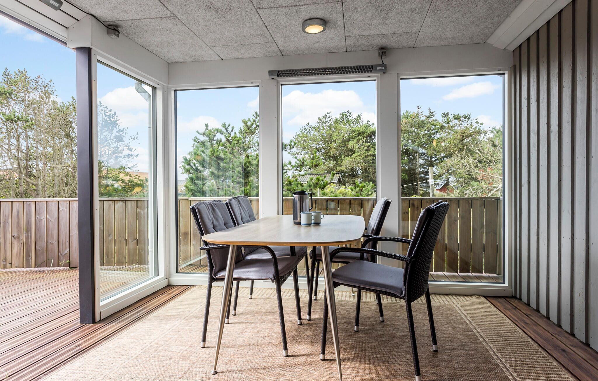 Eine überdachte Terrasse mit Tisch und Stühlen, großen Fenstern und einer Holzterrasse.