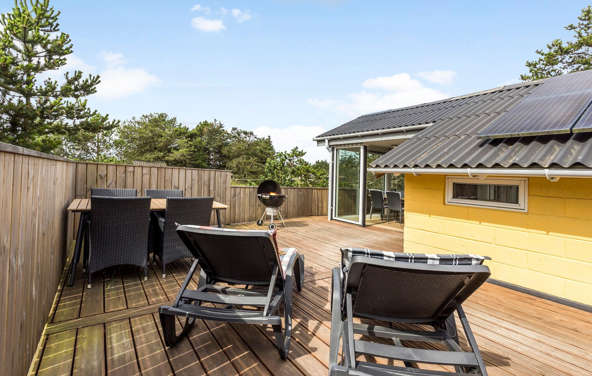 A deck with outdoor furniture, a barbecue grill, and a yellow building with a metal roof.