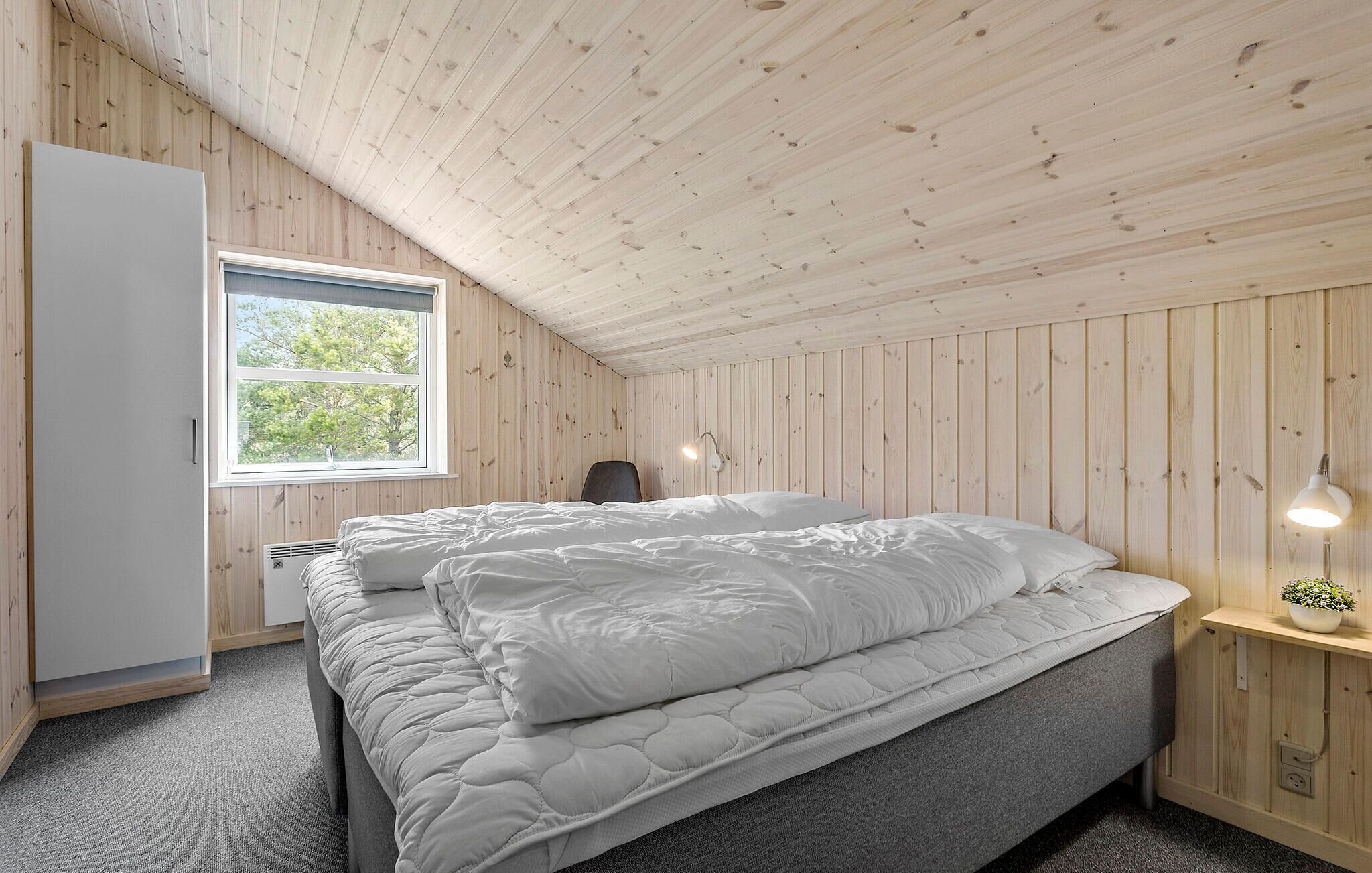 Een slaapkamer met een bed, een raam, een bureau en een lamp.