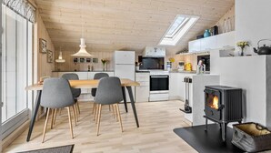 Een moderne keuken met een centraal eiland, een eetgedeelte met grijze stoelen en een houtkachel.