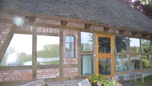 A rustic building with large windows, a wooden door, and a thatched roof. - Reetdachkate on stud Schierensee - Fischerkate (Grebin)