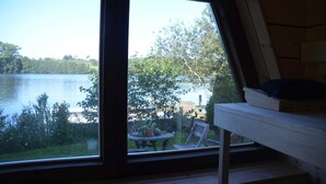 A room with a large window overlooking a lake, a wooden bench, and a small table with a potted plant. - Reetdachkate on stud Schierensee - Fischerkate (Grebin)
