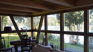 A room with large windows overlooking a lake, wooden furniture, and a table with bottles. - Reetdachkate on stud Schierensee - Fischerkate (Grebin)