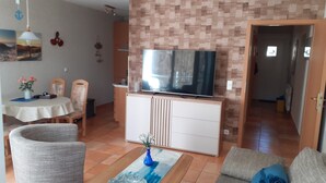 Een woonkamer met een televisie, een eettafel, stoelen en een bank.
