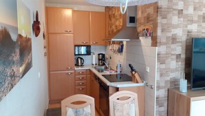 Een kleine keuken met houten kastjes, een magnetron, een waterkoker en een spoelbak.