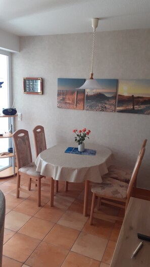 Uma área de refeições com mesa redonda, cadeiras, um vaso com flores e obras de arte nas paredes.