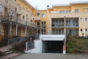 Edifício residencial com várias andares, varandas, entrada coberta e um relógio visível.