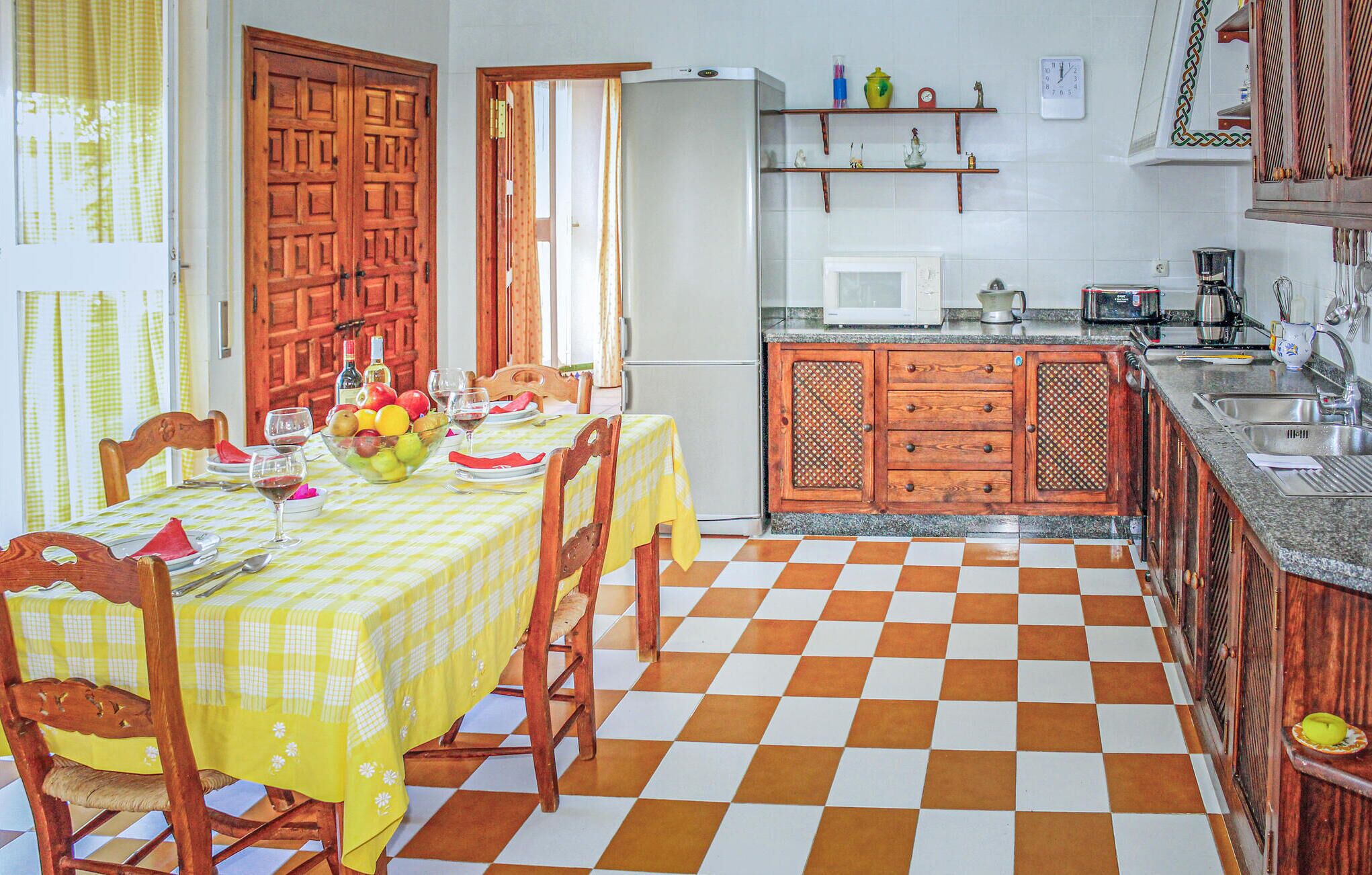 A dining area with a checkered floor, wooden chairs, a table set with plates, glasses, and a fruit bowl.