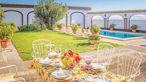 Un espace extérieur aménagé pour les repas, avec une piscine, des chaises en métal blanc et une table dressée pour un repas.