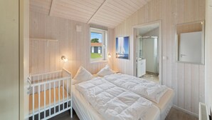 A bedroom with a crib, a large bed, a shower, and a window with a view of a house. - Friedrichskoog-Deichblick 20 (Friedrichskoog)