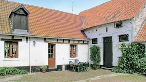 Un edificio tradicional con techo de tejas rojas, paredes blancas y puerta de madera. Cuenta con un pequeño espacio al aire libre con una mesa y sillas.