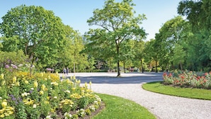 Un parque con un sendero de grava, abundante vegetación y macizos de flores.