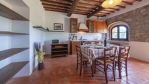 A rustic kitchen with wooden beams, stone walls, and a dining area with a checkered tablecloth. - Cozy apartment in Montecatini V.C. (FI) (Montecatini V.C. (FI))