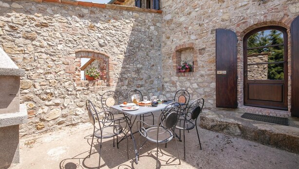 An outdoor stone patio with a table set for dining, surrounded by metal chairs. - Cozy apartment in Montecatini V.C. (FI) (Montecatini V.C. (FI))