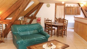 Une pièce chaleureuse avec un canapé en cuir vert, une table à manger en bois et des chaises. On y trouve également un coin cuisine avec des placards en bois et une fenêtre agrémentée de rideaux.