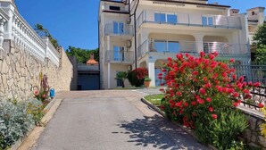 Un edificio a più piani con balconi, un muro in pietra e un giardino curato con fiori rossi.