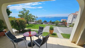 Una terrazza con un tavolo rotondo e quattro sedie, una pianta in vaso e vista sul mare e sugli edifici.